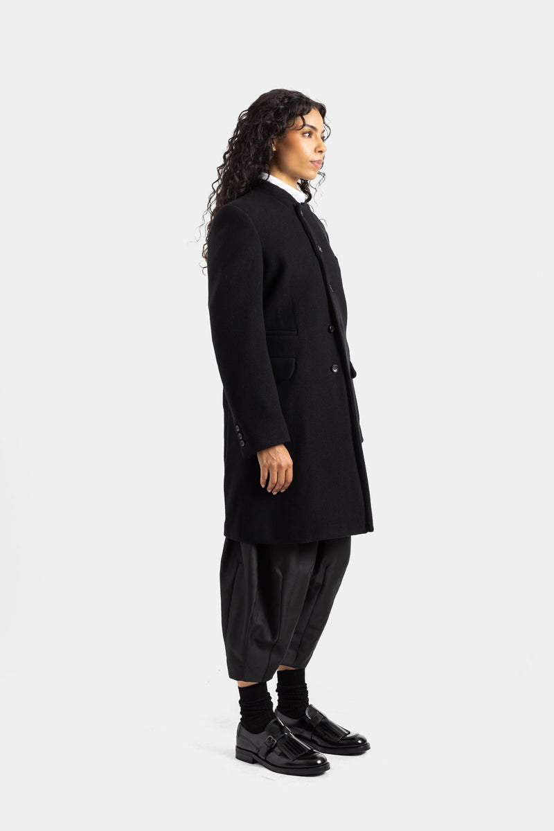 Abrigo de lana negra Comme des Garçons para mujer de perfil con botonadura simple y pantalón de harén.
