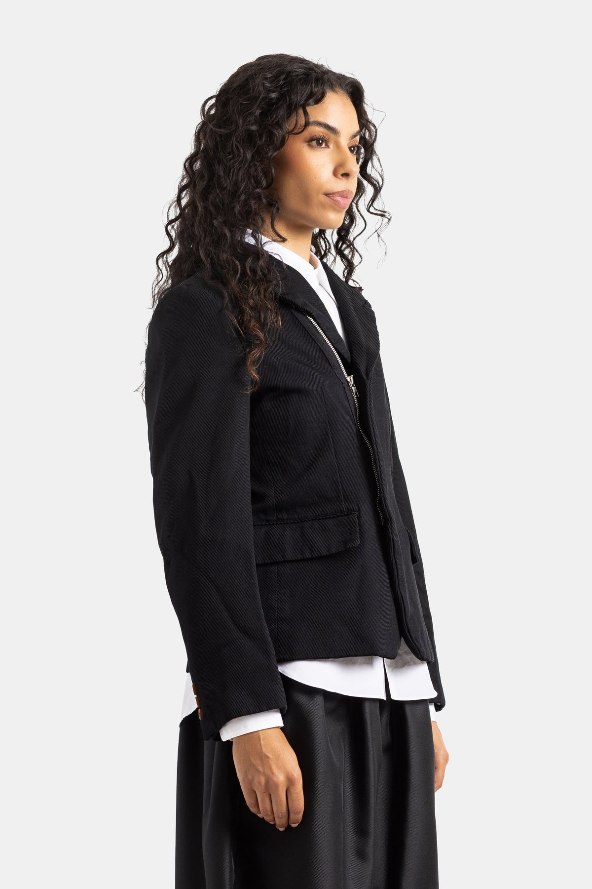 Chaqueta negra acolchada Comme des Garçons de perfil, con cierre de cremallera diagonal sobre camisa blanca