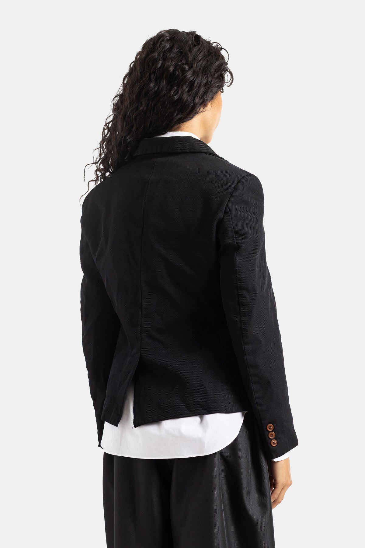 Chaqueta de sastre negra Comme des Garçons vista trasera, botones caramelo en manga, corte corto y sutil