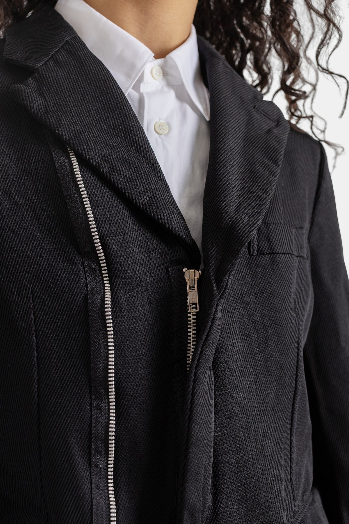 Primer plano de chaqueta Comme des Garçons con cremallera asimétrica y tirador de metal sobre sarga