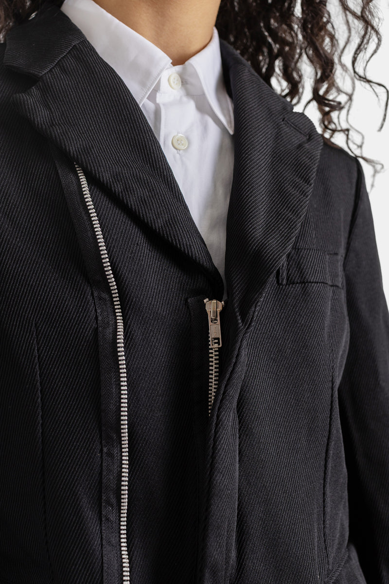 Primer plano de chaqueta Comme des Garçons con cremallera asimétrica y tirador de metal sobre sarga