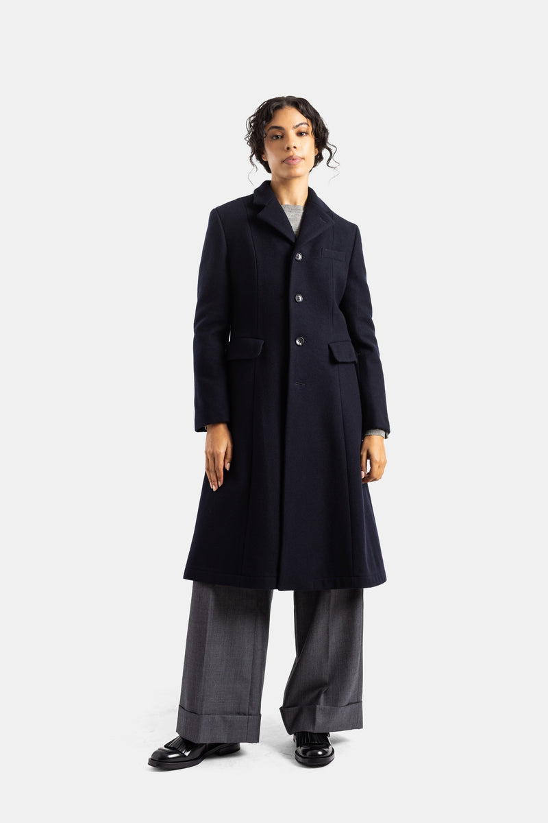 Abrigo largo de mujer Comme des Garçons en lana azul marino con pantalón ancho gris y mocasines negros.