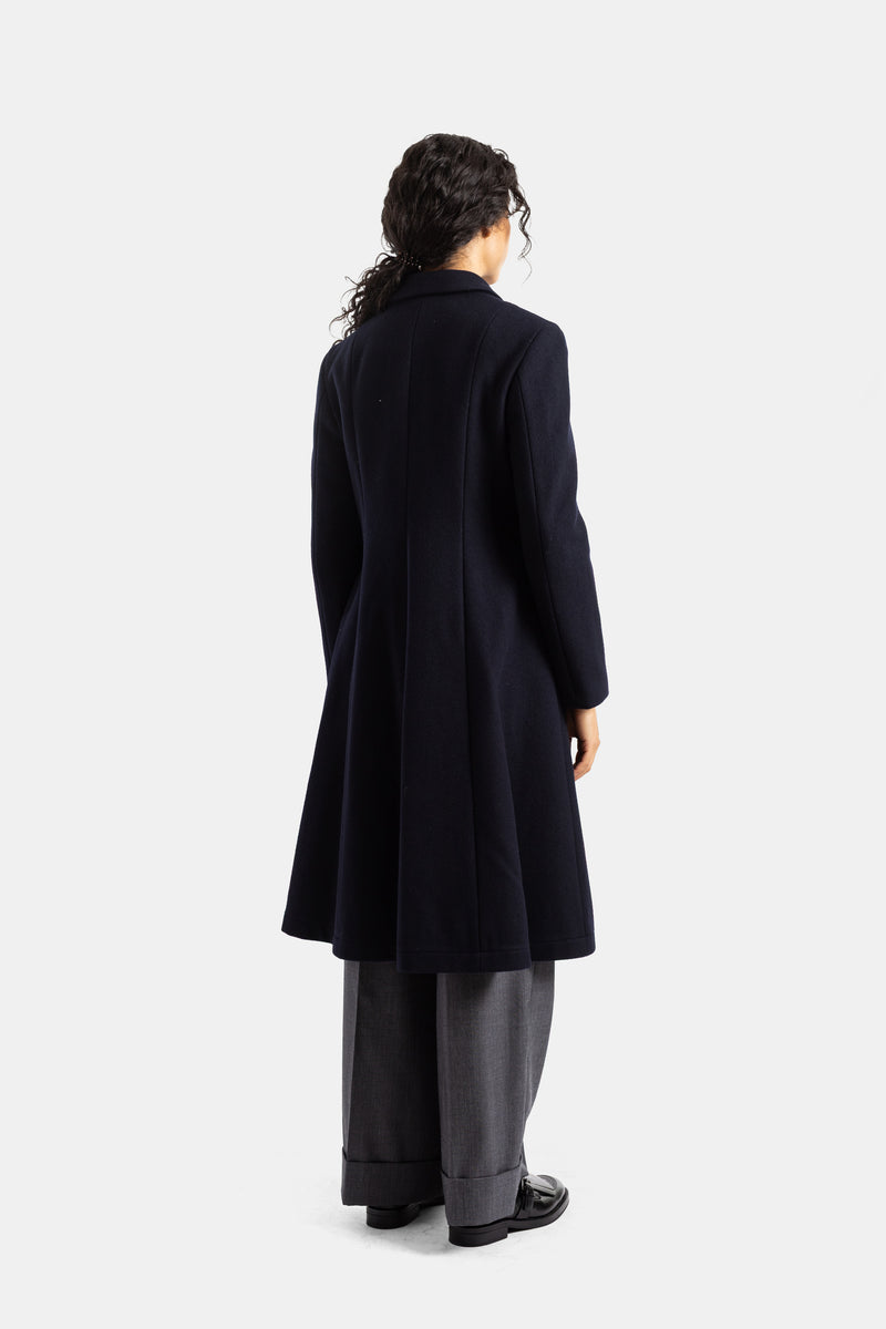 Vista trasera del abrigo de lana azul marino Comme des Garçons con cortes verticales y bajo acampanado.