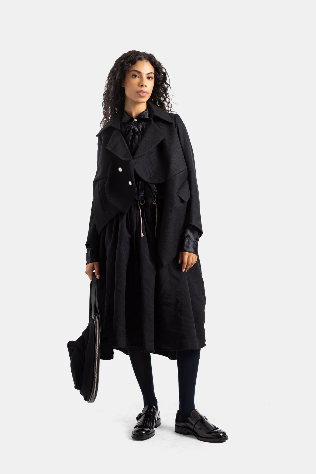 Chaqueta negra estructurada Comme des Garçons en look total black con mocasines de charol y bolso de mano