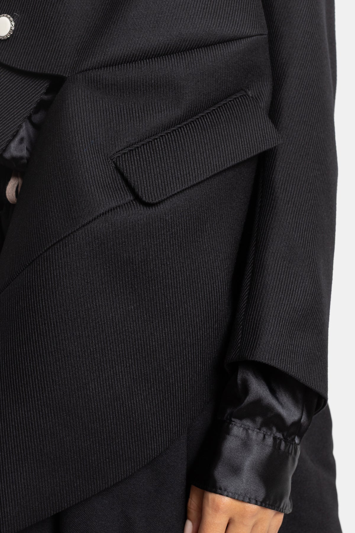Detalle de bolsillo con solapa en chaqueta Comme des Garçons de lana negra acanalada y puño asimétrico
