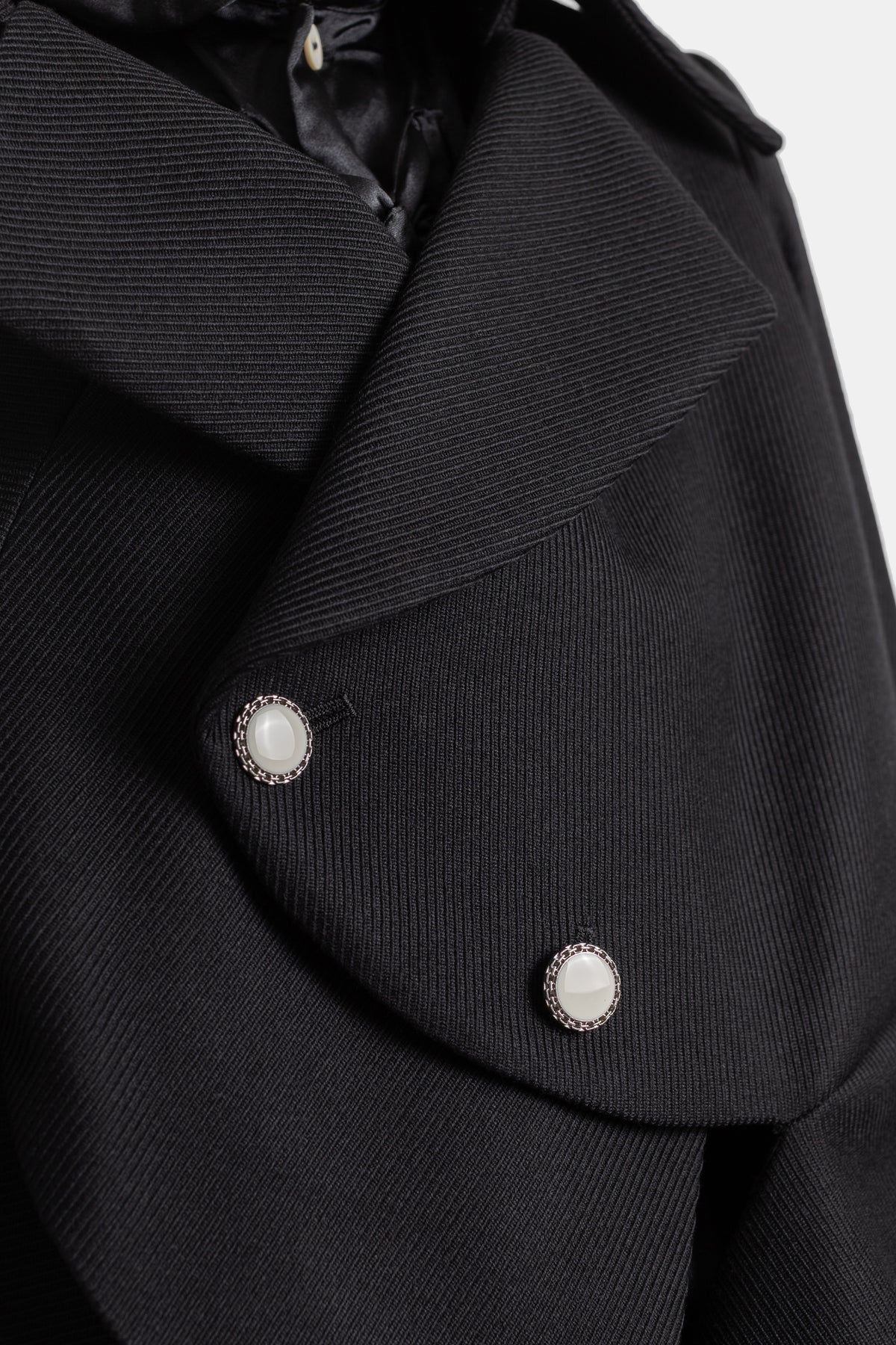 Primer plano de chaqueta negra Comme des Garçons con botones nacarados plateados y cuello superpuesto