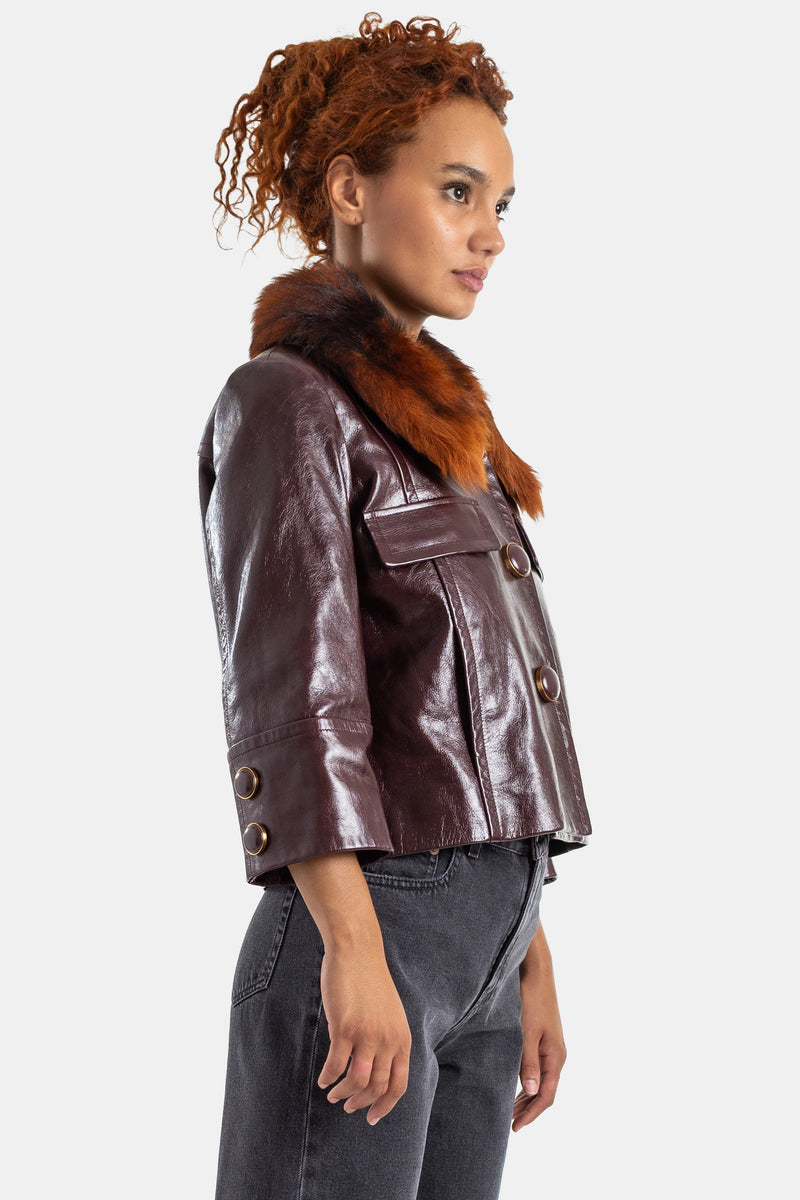 Chaqueta Chloé de charol burdeos, vista de perfil, cuello de piel pelirroja, botones de metal bronce, mujer.