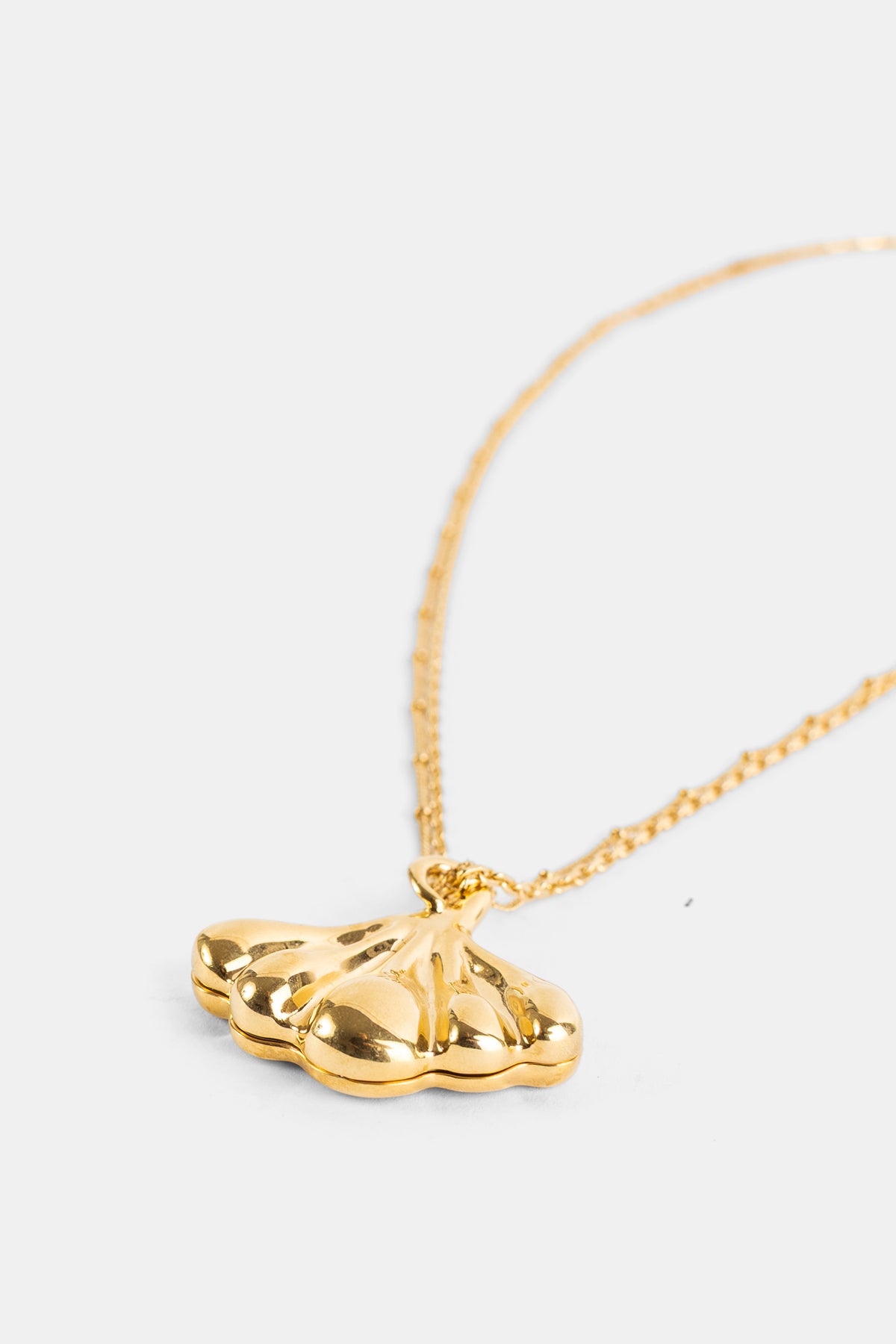 Chloé pendentif laiton doré forme ail sculptée, reflets brillants sur fond blanc, vue de côté rapprochée