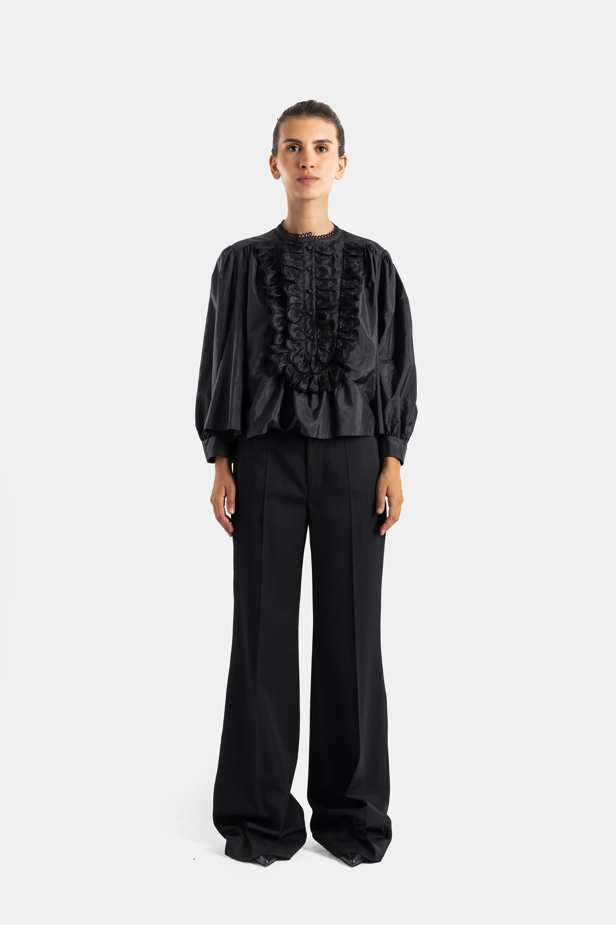 Chloé blouse noire portée avec un pantalon large, détails jabots superposés et manches volumineuses à poignets resserrés