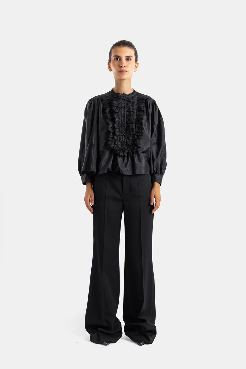 Chloé blouse noire portée avec un pantalon large, détails jabots superposés et manches volumineuses à poignets resserrés