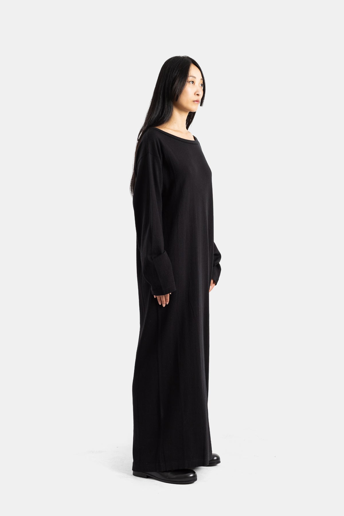 Extreme Cashmere black cashmere maxi dress in profile, showing a fluid ankle-length silhouette with black shoes.