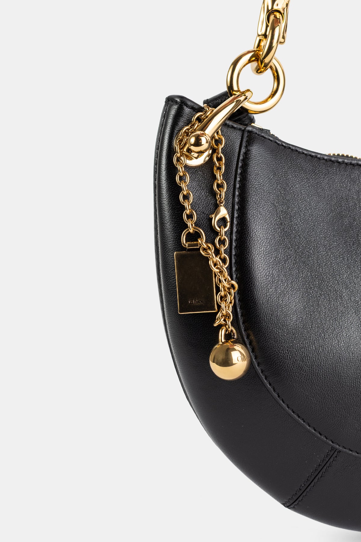 Chloé Banana gros plan quincaillerie dorée, chaîne fine à pendentif sphère et plaque logo sur cuir noir