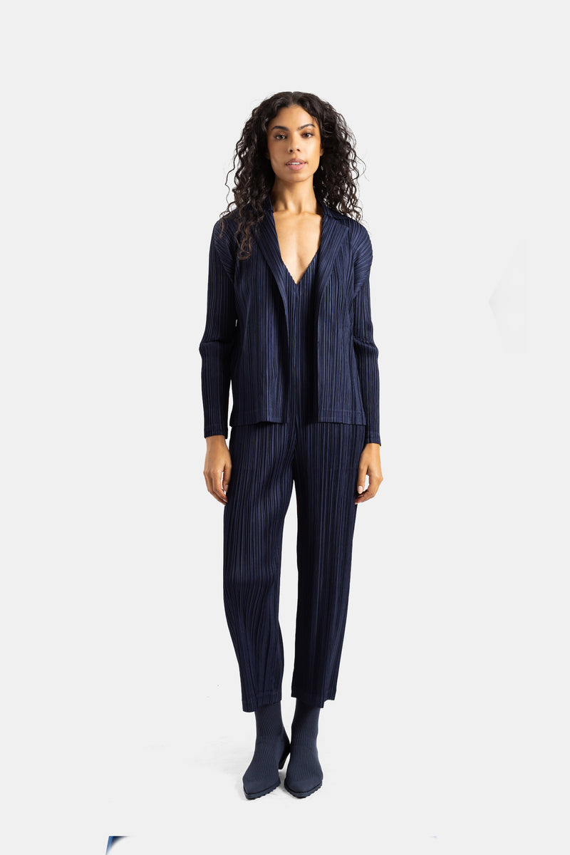 Pleats Please Issey Miyakeのディープネイビーのプリーツジャケットとストレートパンツの女性用コーディネート。正面から捉えた、流れるような美しいシルエットと統一感のあるモダンなグラフィックススタイル。