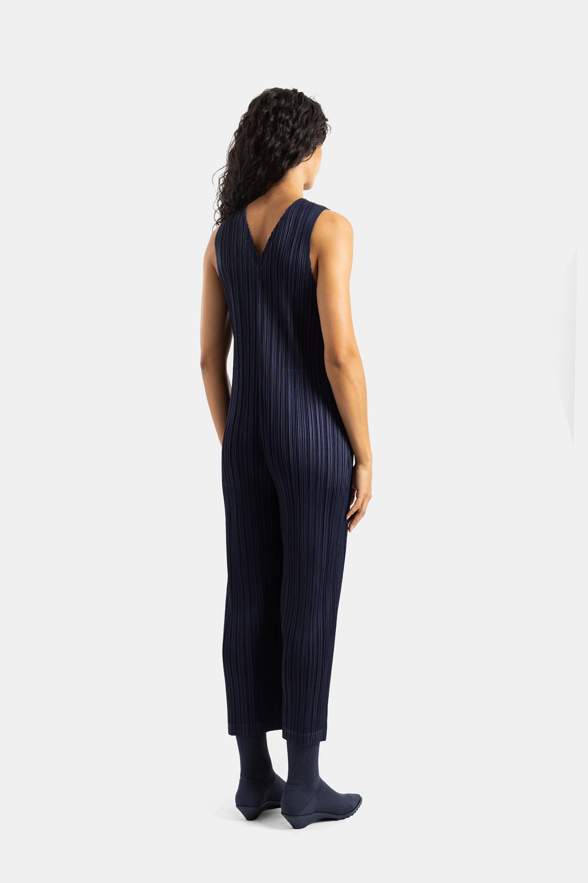 Tuta Pleats Please Issey Miyake scollo a V plissé blu notte vista posteriore con scarpe e calze coordinate