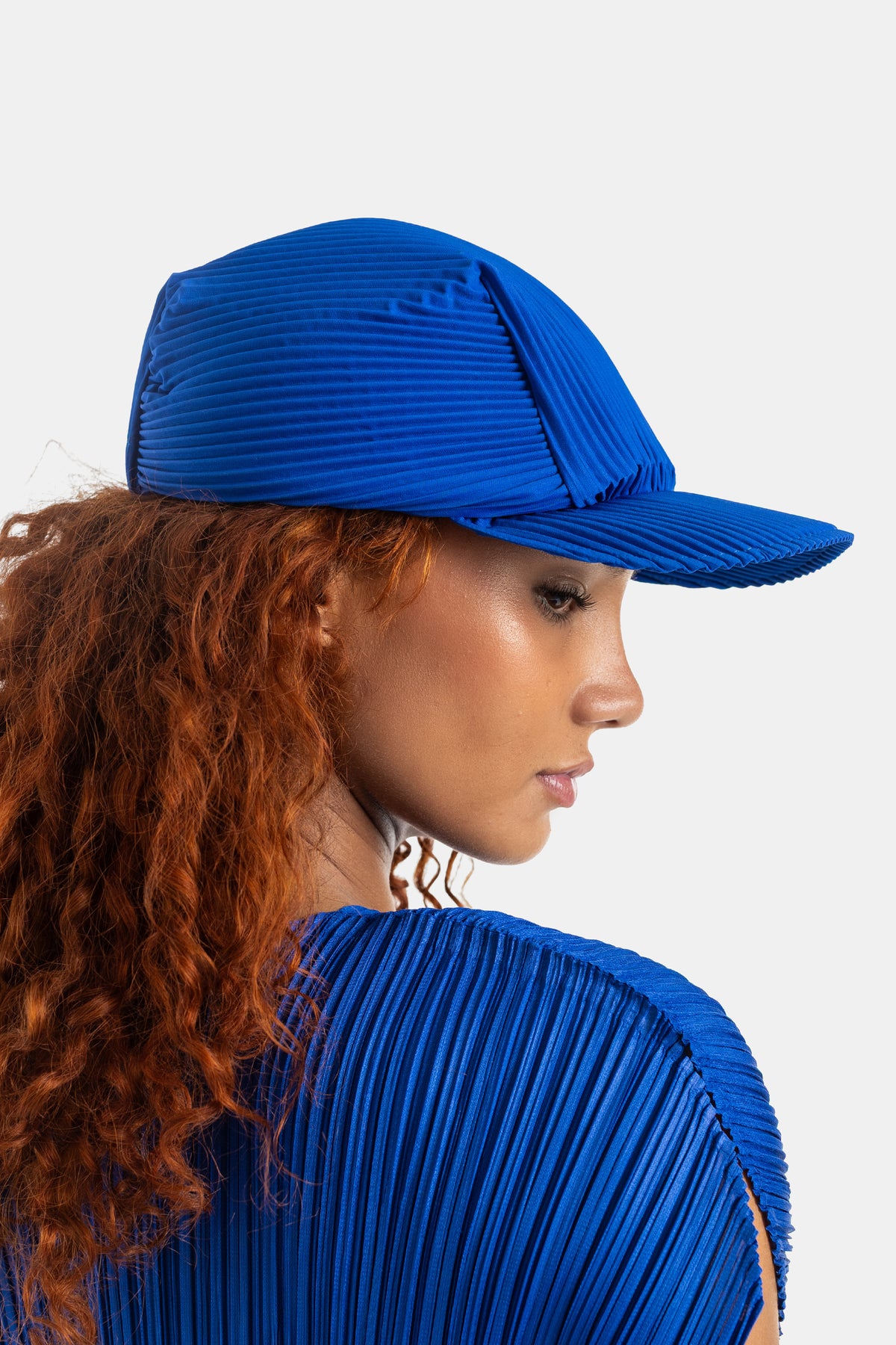Pleats Please Issey Miyake casquette et top plissés bleu roi coordonnés vue trois-quarts dos cheveux roux