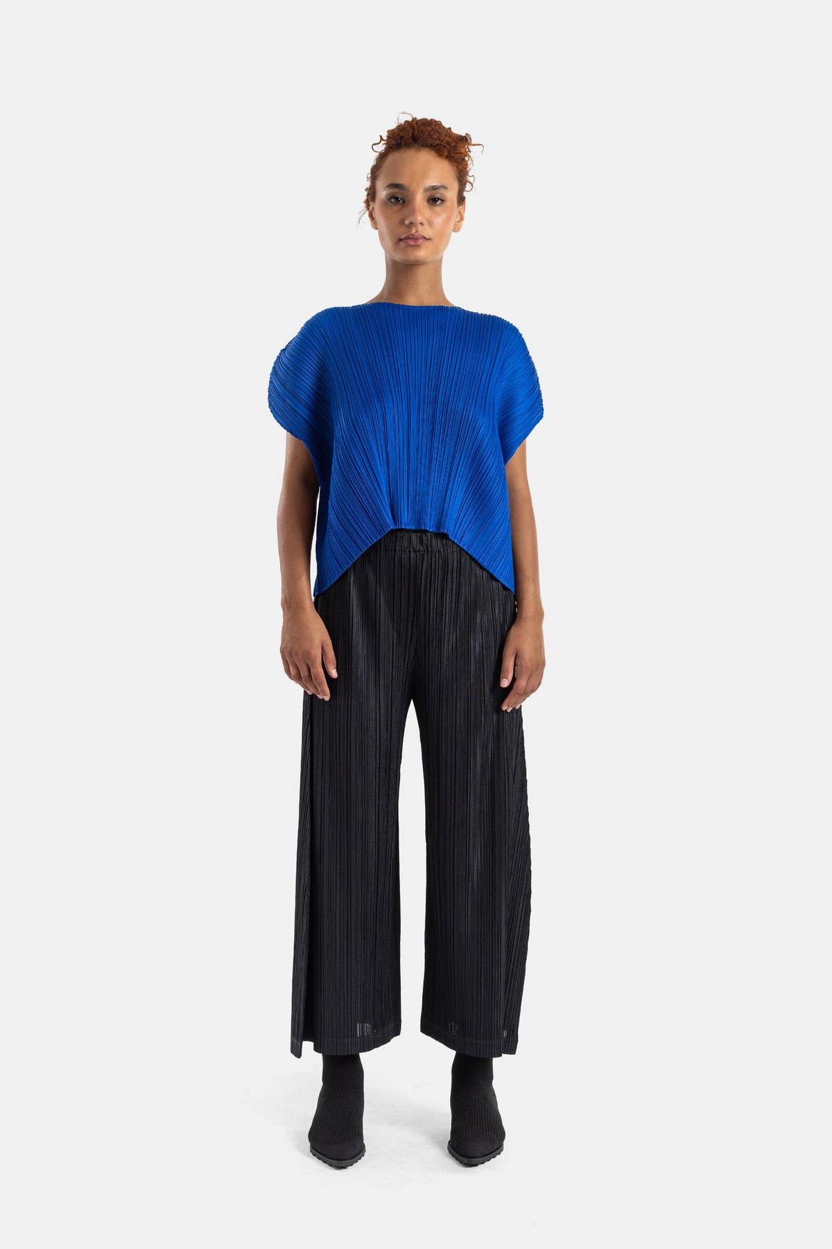 Pantalón plisado negro de Pleats Please Issey Miyake combinado con un top azul cobalto para mujer