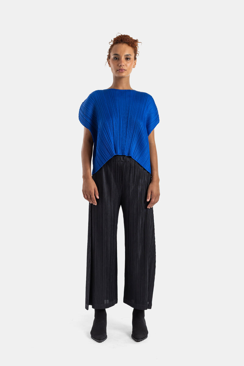 Pantalón plisado negro de Pleats Please Issey Miyake combinado con un top azul cobalto para mujer