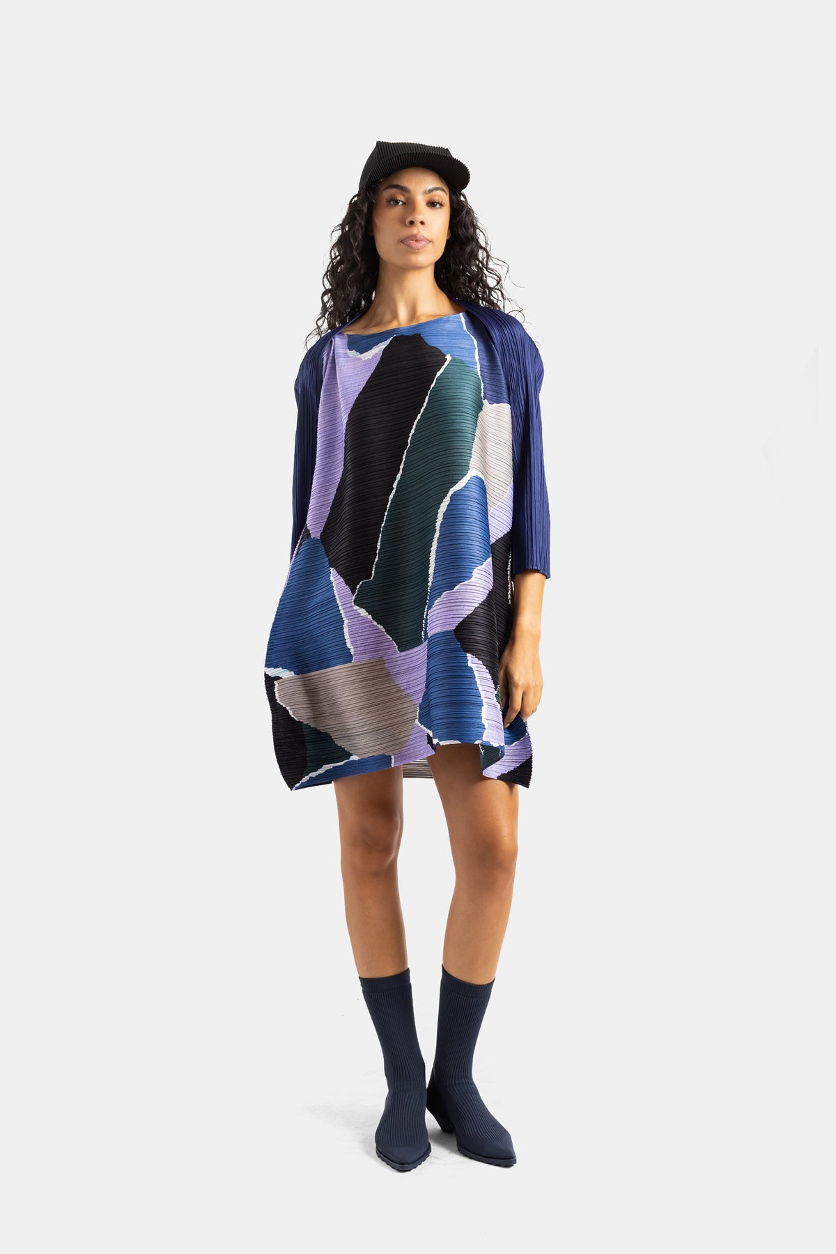 Pleats Please Issey Miyake geplisseerde jurk, complete look met pet, sokken, blauwe laarzen, microplissé textuur.