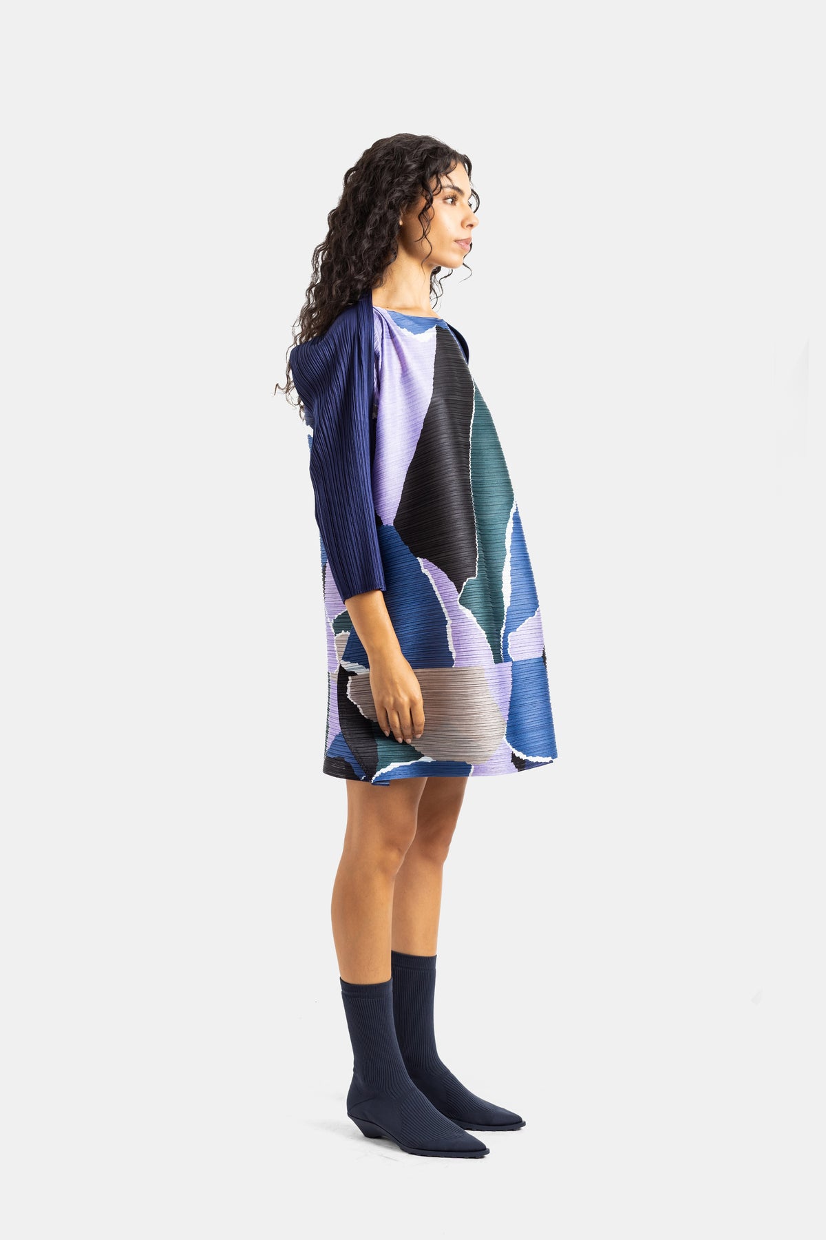 Pleats Please Issey Miyake korte jurk in profiel, uitlopend silhouet met groot geometrisch kleurrijk motief.