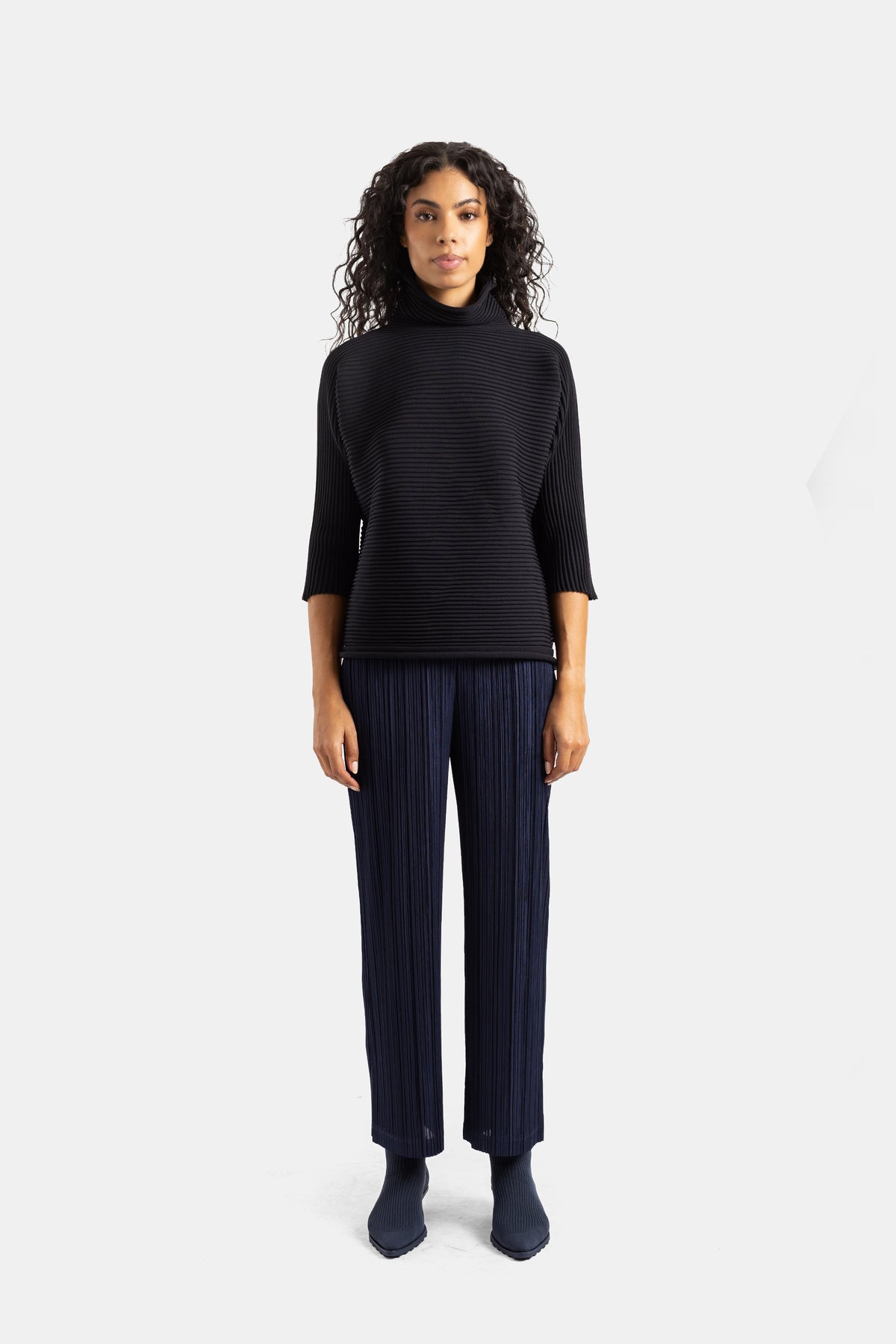Top de gola alta preto Pleats Please Issey Miyake com calças azuis plissadas, conjunto coordenado feminino.