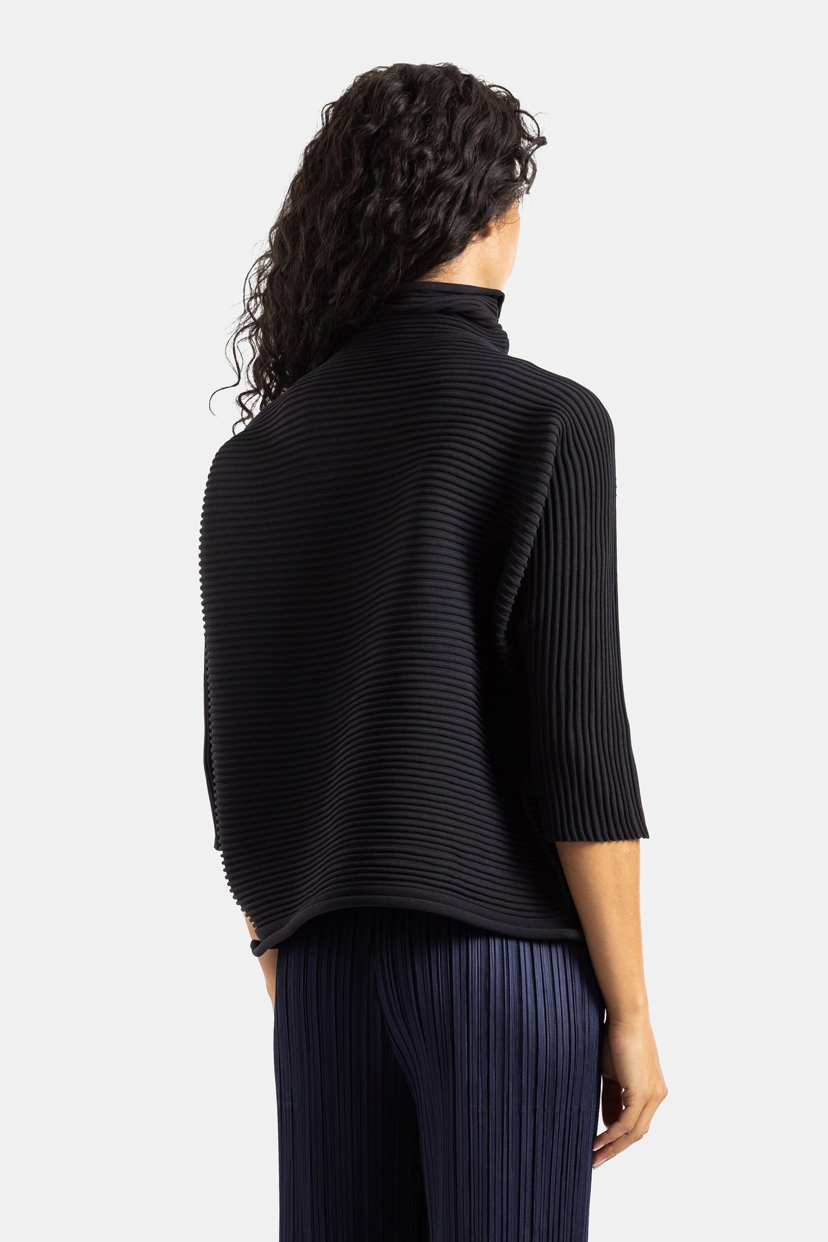 Top preto Pleats Please Issey Miyake visto de costas, plissado canelado estruturado e corte boxy evasê.