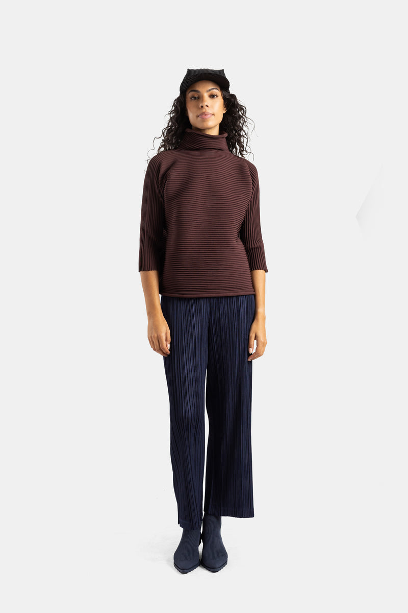 Conjunto Pleats Please Issey Miyake con top marrón chocolate, pantalón plisado azul marino y botines a juego