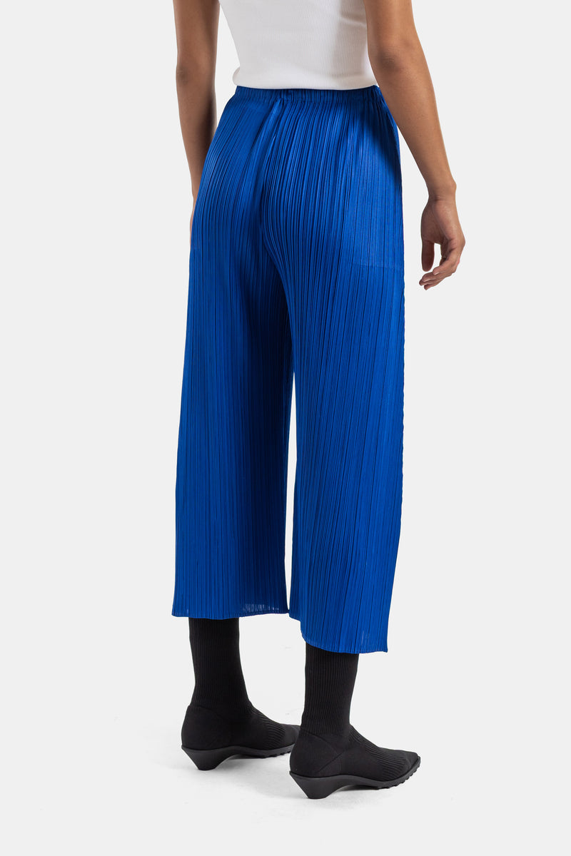 Pleats Please Issey Miyake plissé broek in felblauw, achteraanzicht met elastische taille en wijde broekspijpen.