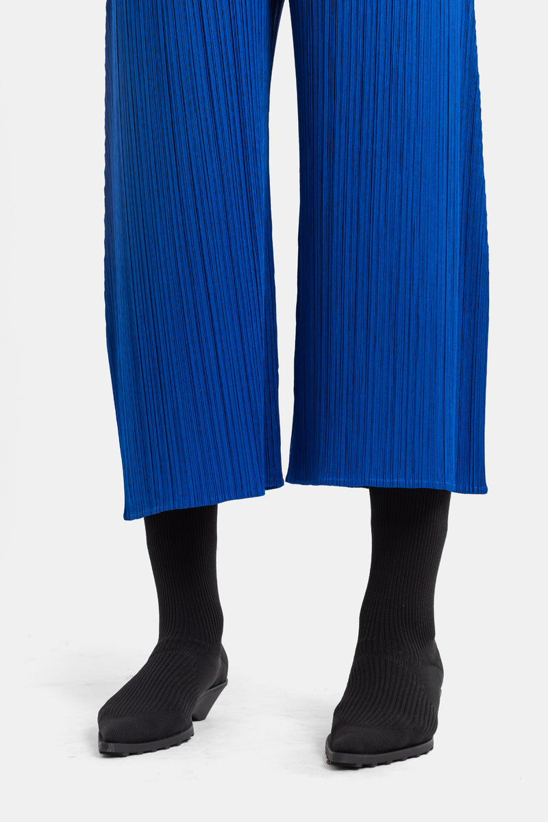 Pleats Please Issey Miyake satijnblauwe plissé broek, detail van de wijde zoom gecombineerd met zwarte soklaarsjes.
