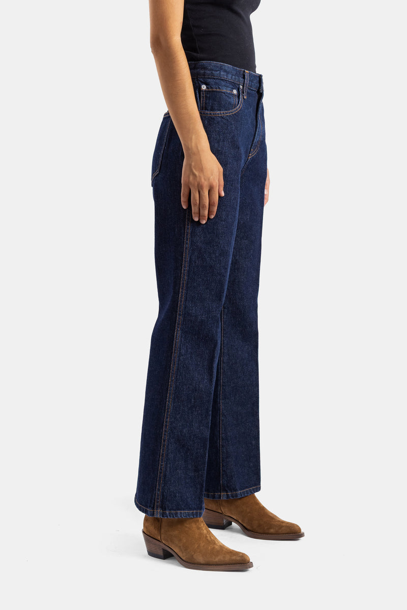 Khaite jean Clara coupe évasée vue de profil, denim brut indigo foncé porté avec bottines en daim camel