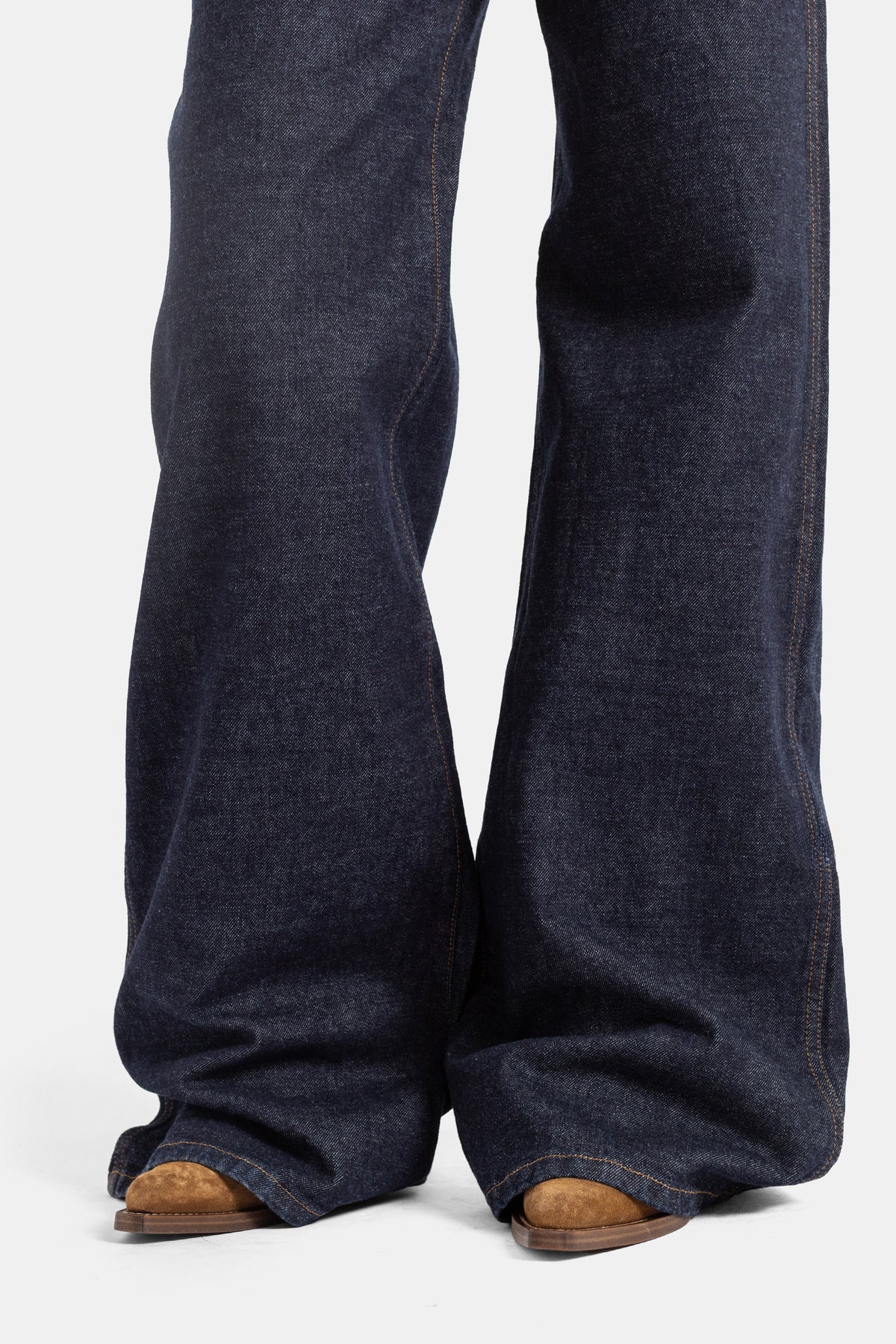 Khaite jean Dane bas de jambe évasé denim brut indigo, ourlet long sur boots camel, coupe flare volume