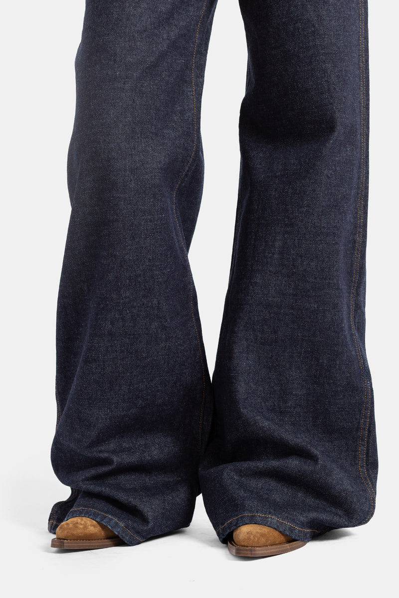 Khaite jean Dane bas de jambe évasé denim brut indigo, ourlet long sur boots camel, coupe flare volume