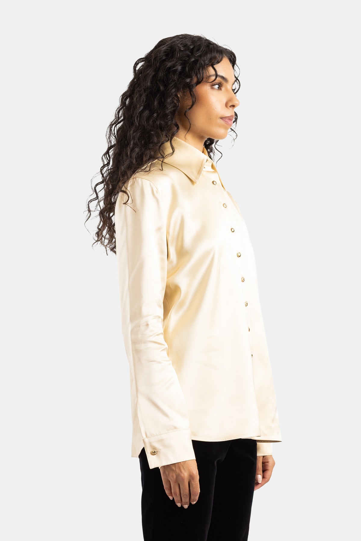 Blusa Ivy Khaite in raso avorio di profilo con polsini dotati di bottoni dorati e silhouette femminile sagomata.