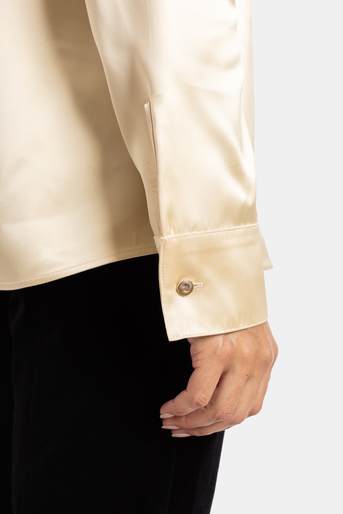 Polsino della camicia Ivy Khaite in raso champagne abbottonato con fermaglio dorato inciso su pantaloni in velluto.
