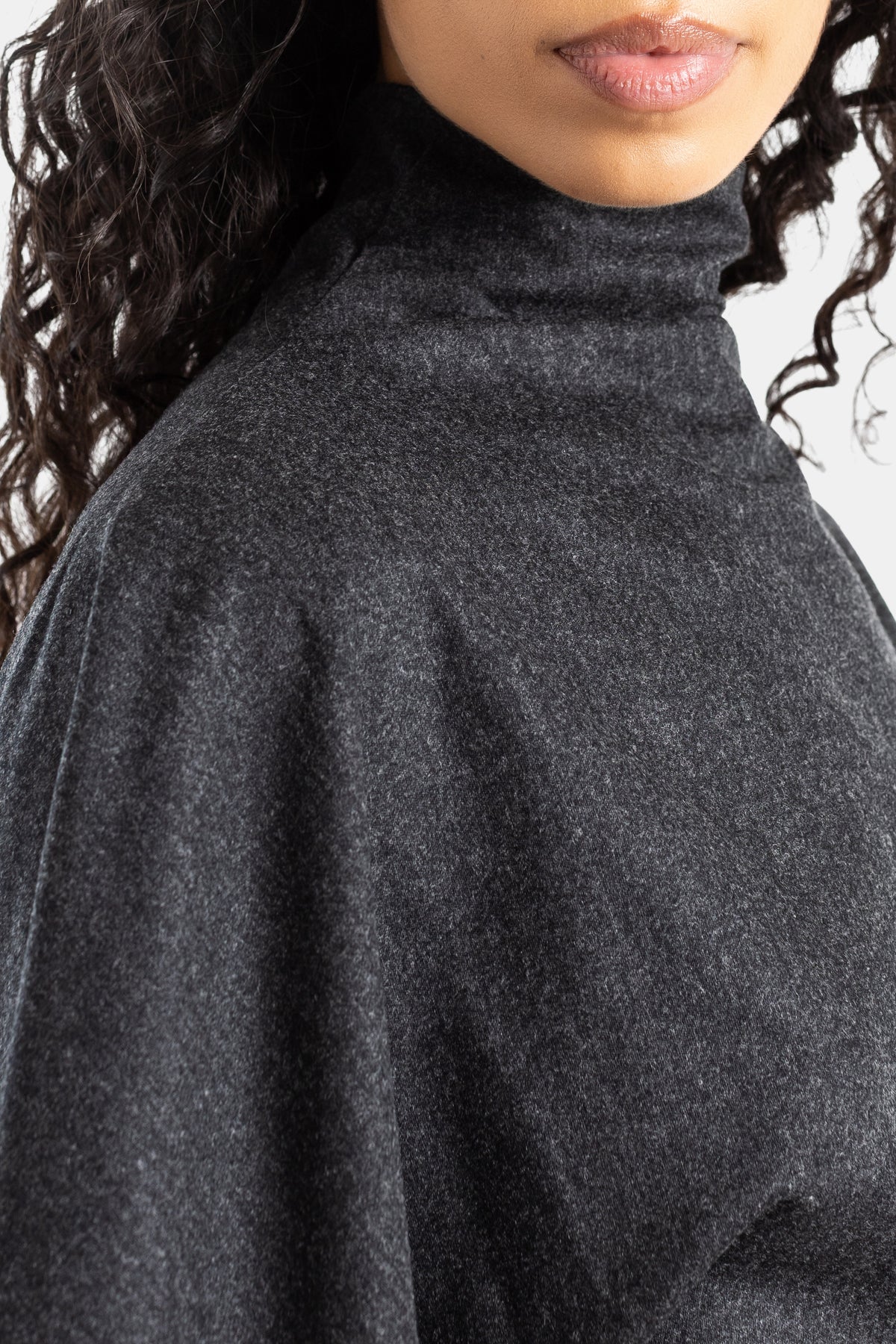 Detail van de Khaite Harlin-jurk met gedrapeerde col in antracietgrijze wol, soepel vallende mouwen.