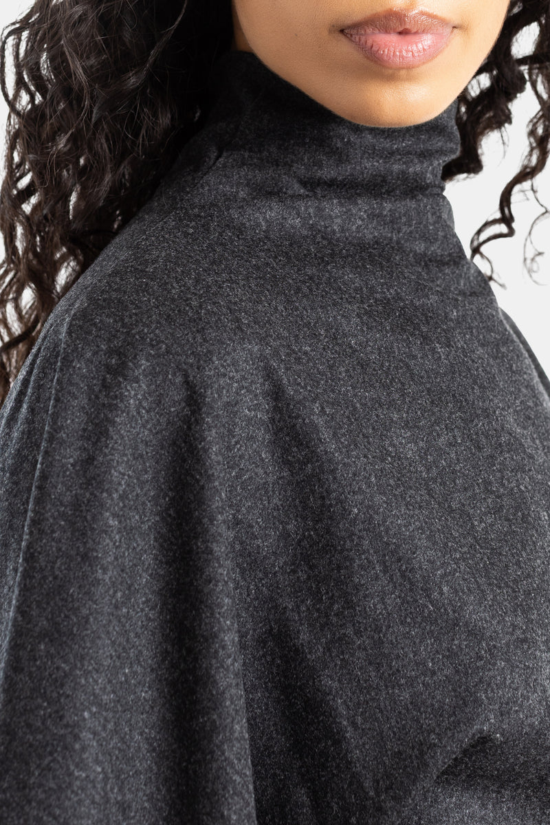 Detail van de Khaite Harlin-jurk met gedrapeerde col in antracietgrijze wol, soepel vallende mouwen.