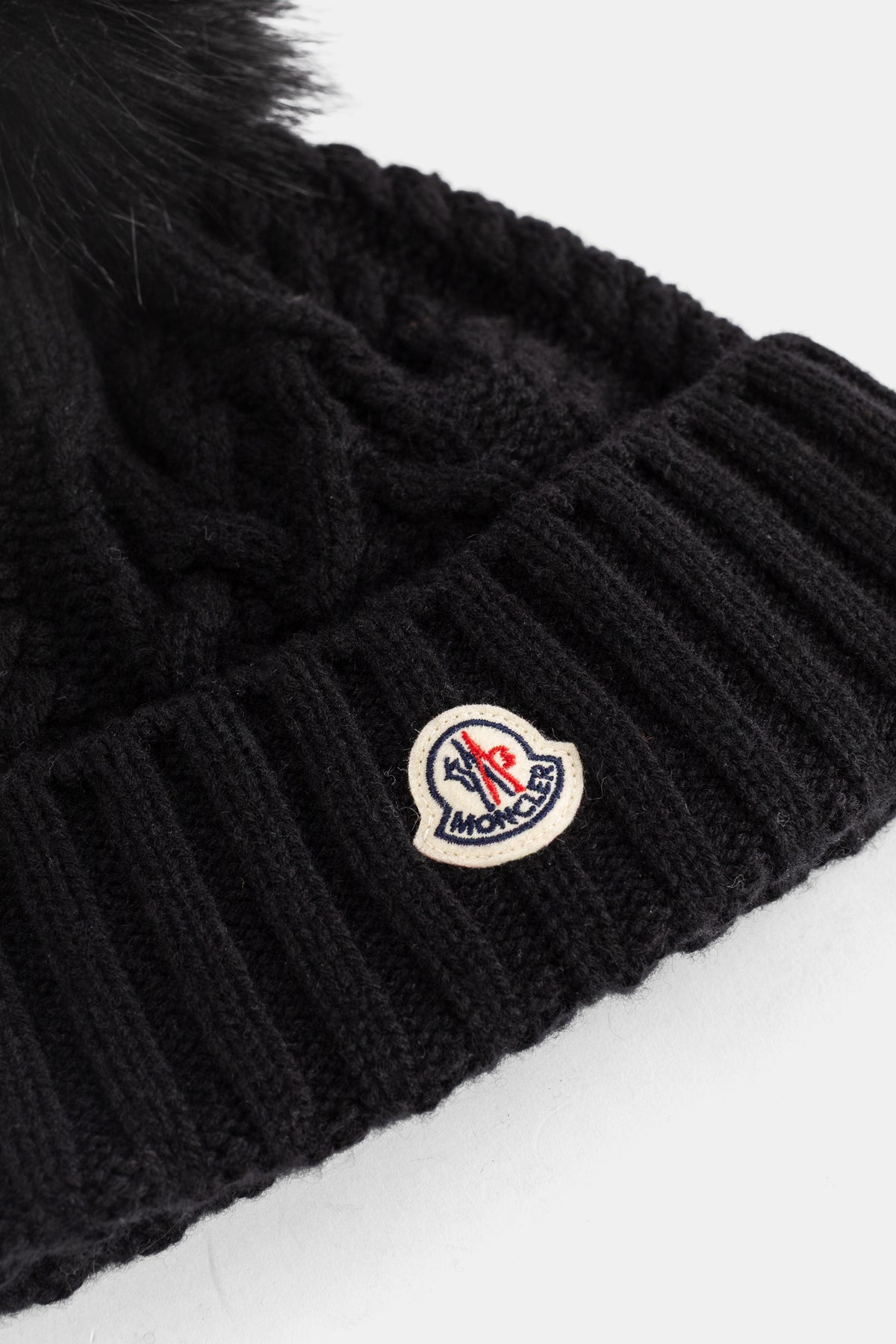 Détail du patch logo Moncler brodé sur bonnet femme noir côtelé avec pompon fourrure