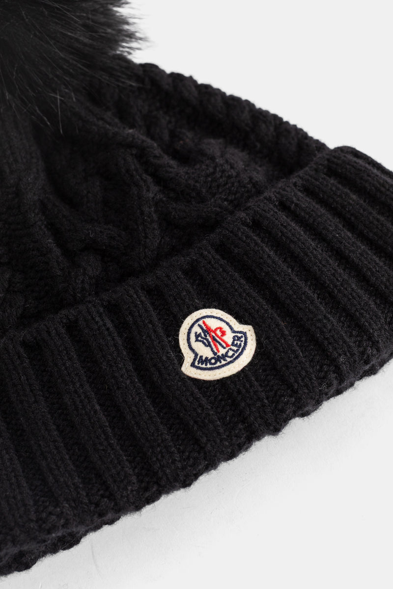 Close-up of the embroidered Moncler logo patch on this women's black ribbed beanie with a fur pompom.