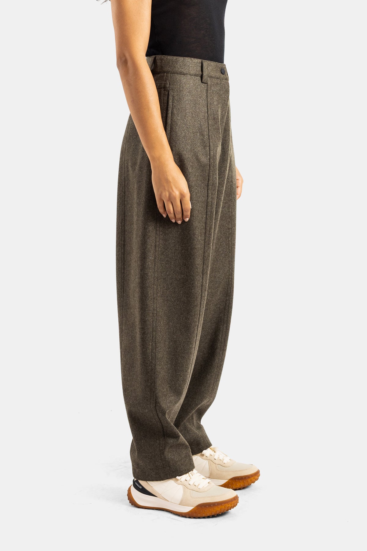 Pantalón de lana caqui Moncler Grenoble en vista de perfil con corte amplio, pliegues y zapatillas de deporte.