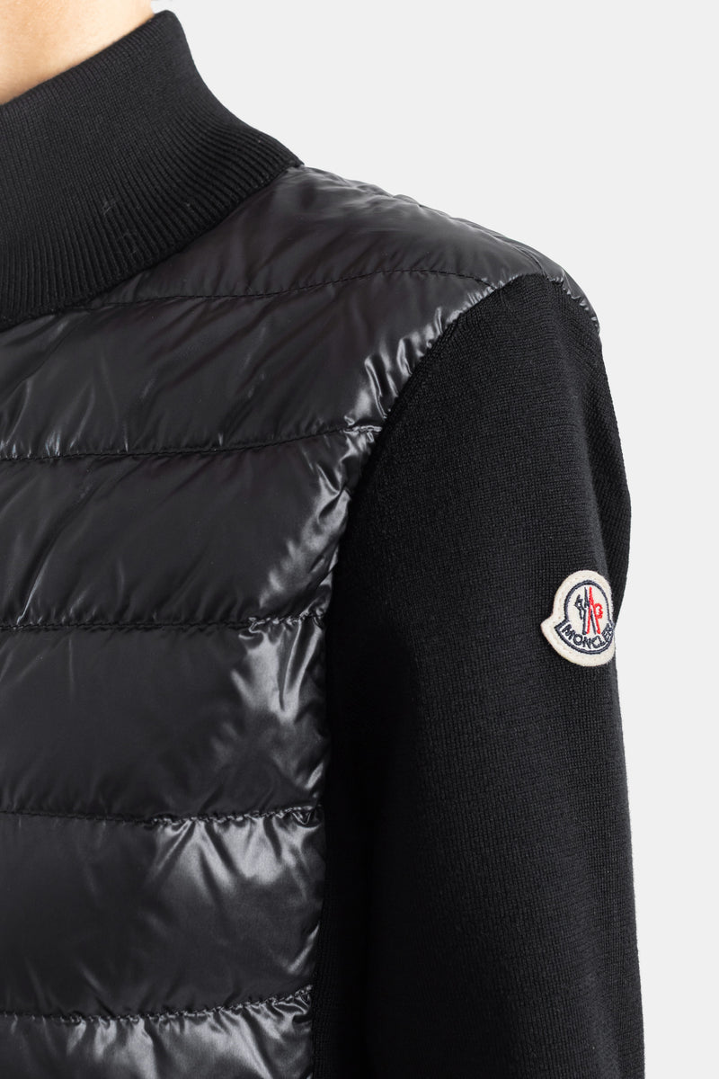 Detalle del parche con logotipo Moncler en el hombro de chaqueta híbrida acolchada de nylon y punto negro.