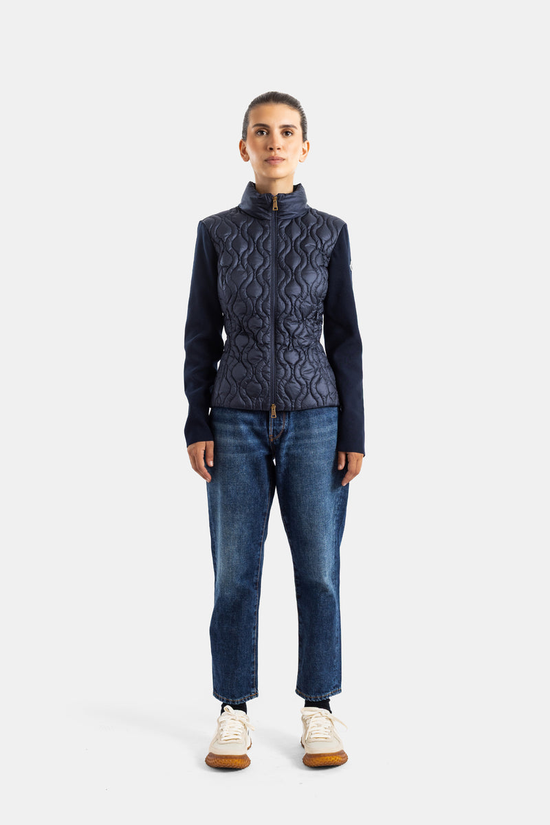 Vista frontal do cardigan híbrido Moncler para mulher em azul-noite acolchoado, com jeans retos e sapatilhas brancas.