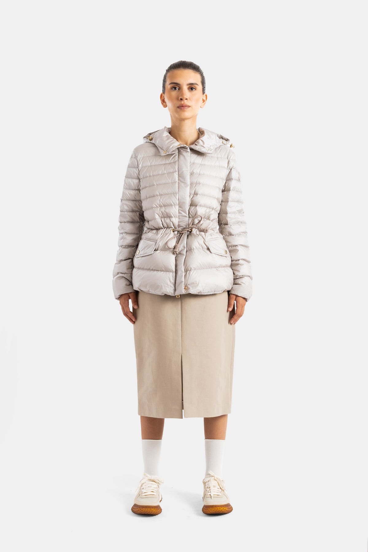 Moncler women's down jacket, front view, drawstring waist, gold cords, beige midi skirt, white sneakers