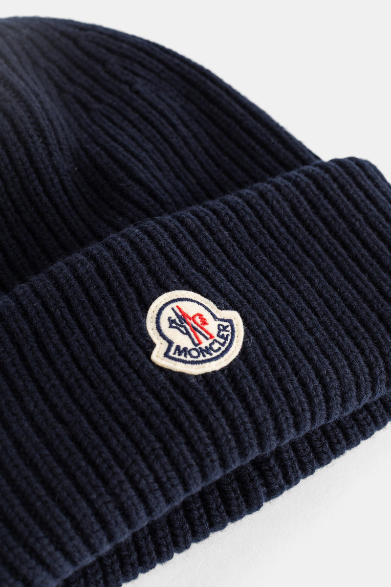 Detalle del parche de logotipo Moncler en gorro de hombre de punto acanalado azul marino con lana virgen visible.