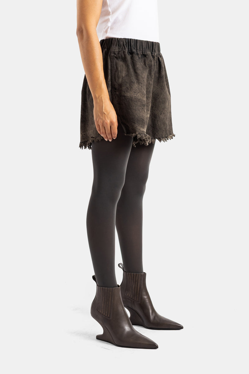 Shorts in denim marrone Rick Owens con collant scuri e stivaletti con tacco biseautato, vista di profilo.