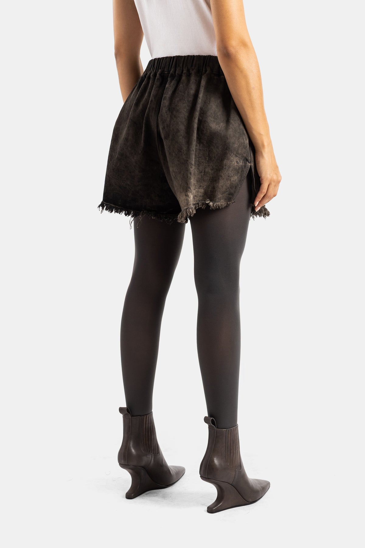Retro degli shorts in denim délavé Rick Owens con orlo sfrangiato, vita elastica, collant e stivaletti marroni.