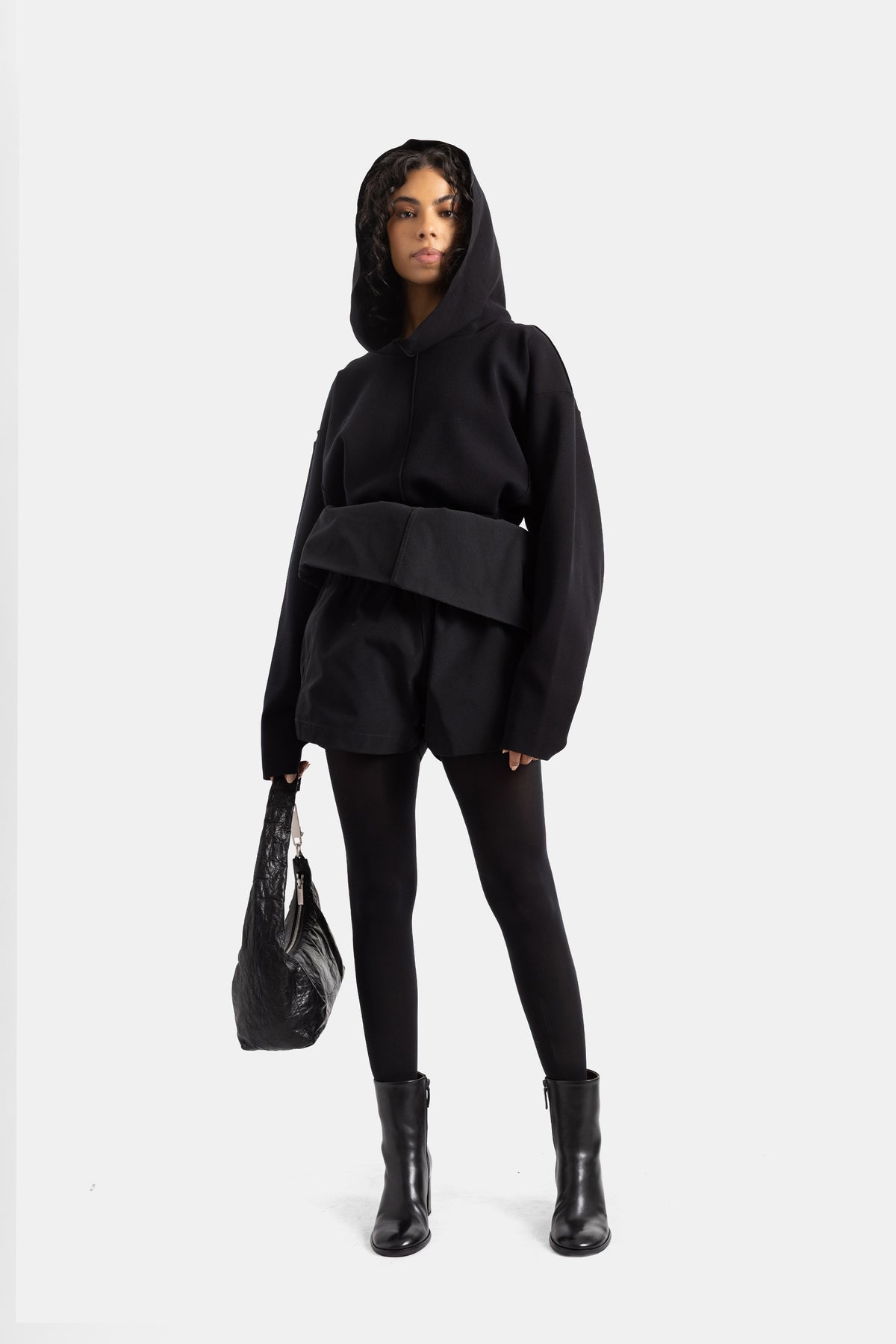 Front view of women's black Rick Owens playsuit with hood and wide crossed belt worn over black leggings