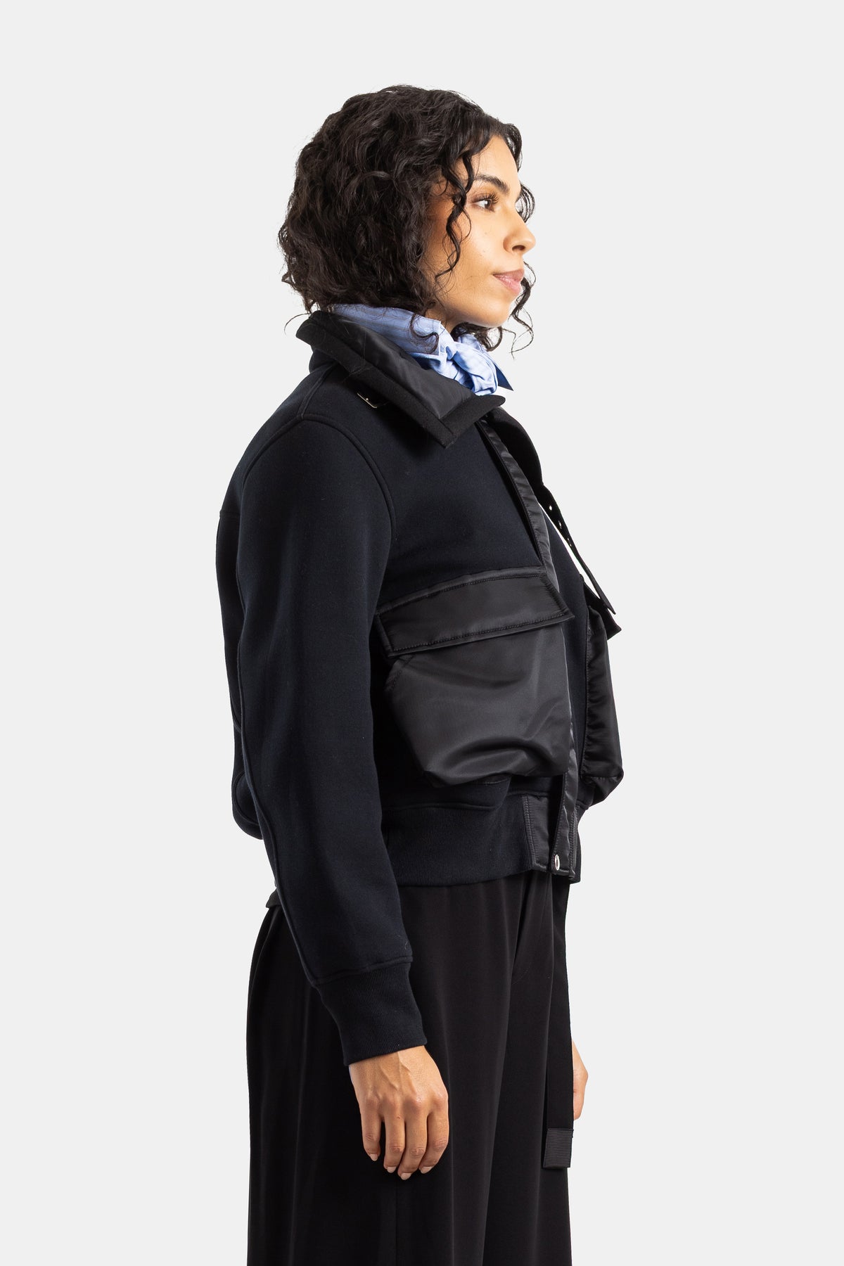 Sacai women's profile black jacket featuring a large nylon cargo pocket and a sky blue scarf at the collar