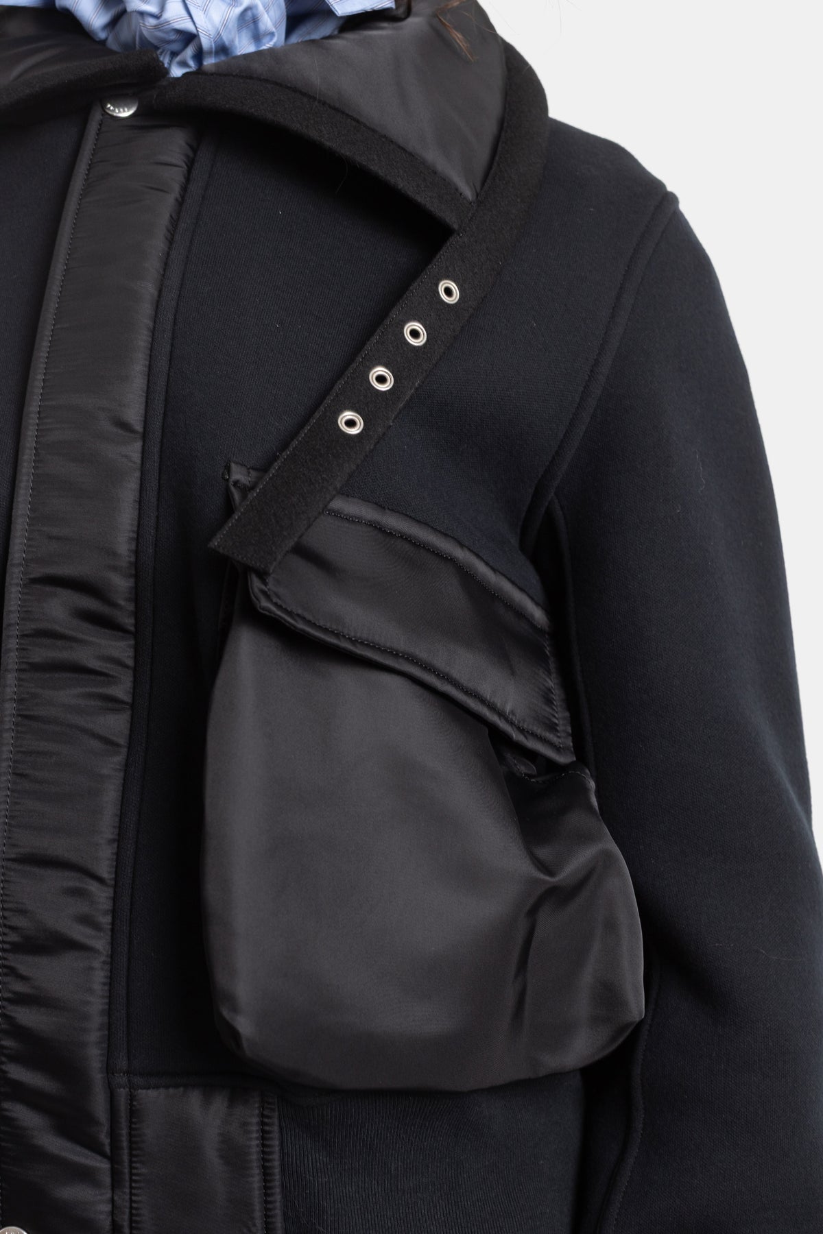 Sacai black jacket close-up on satin nylon cargo pocket with silver eyelets and crossed neoprene strap