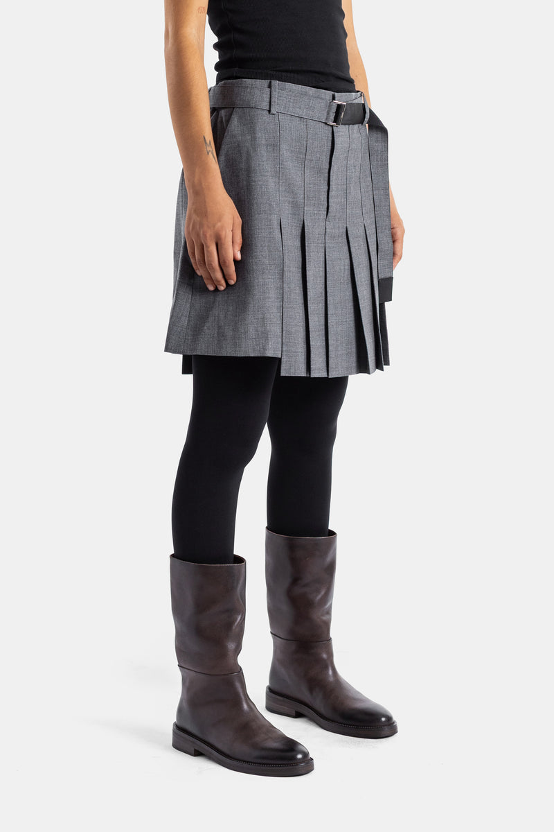 Sacai short-jupe plissé gris porté avec collants noirs et bottes cuir marron, vue de profil