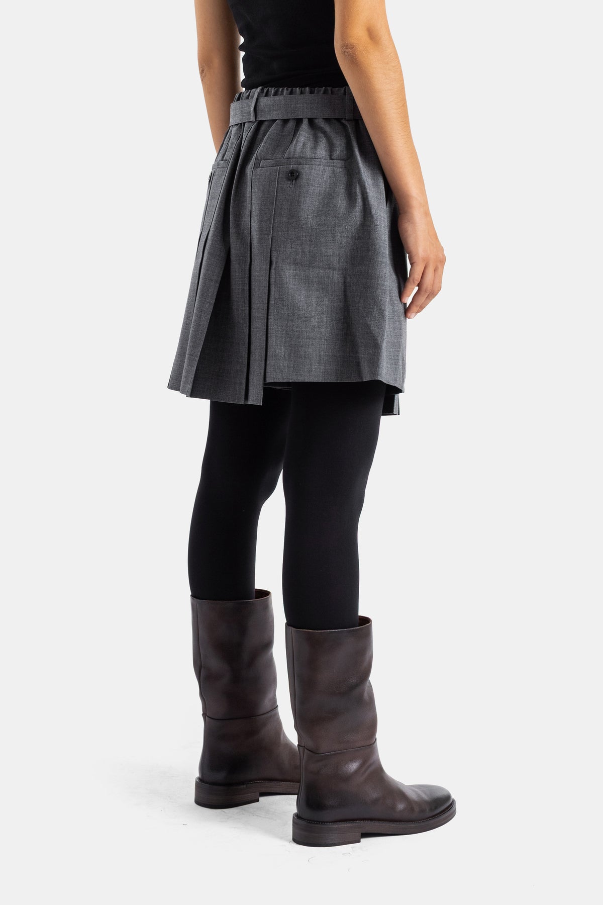 Sacai short-jupe laine grise, détail dos avec poche et bouton, porté sur collants noirs et bottes cuir