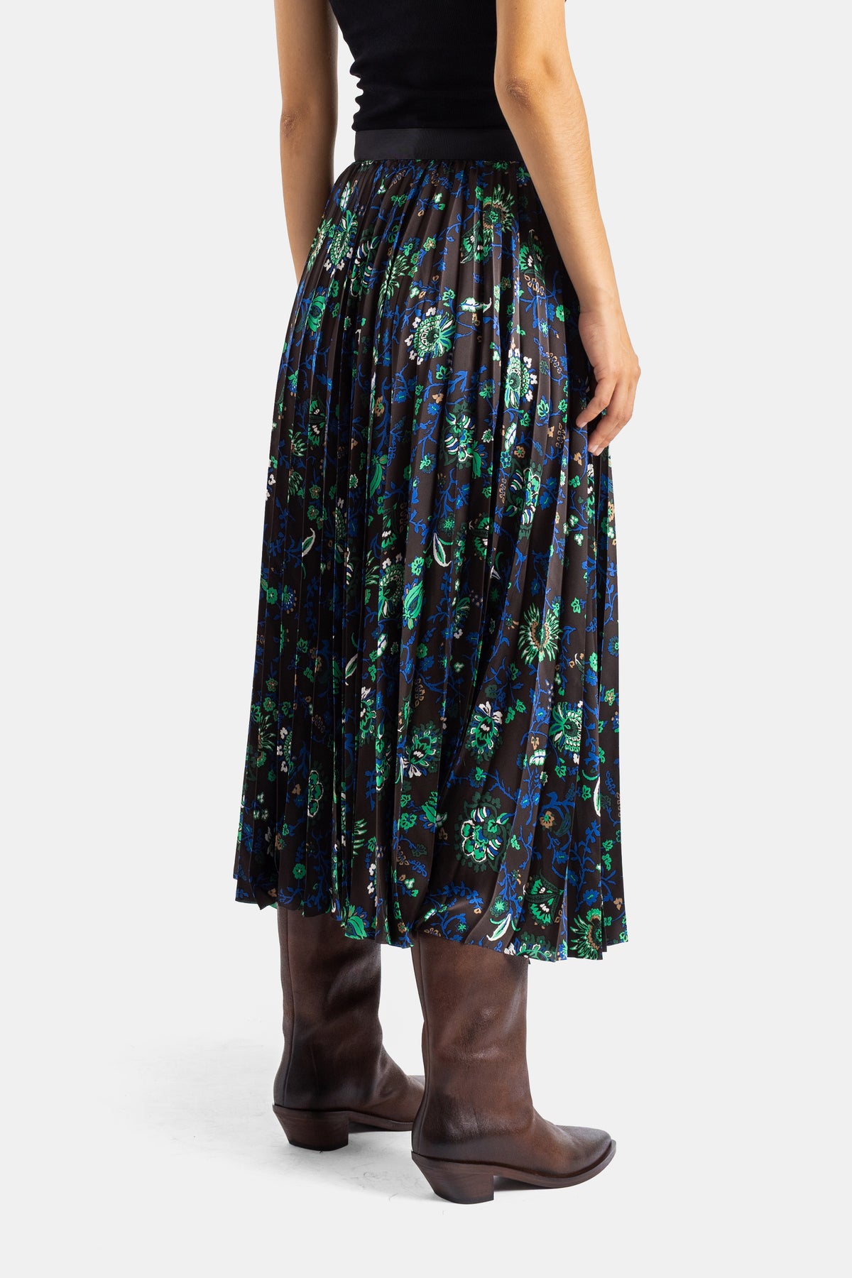 Sacai jupe plissée mi-longue dos, imprimé floral vert bleu sur fond sombre, portée avec bottes cuir marron